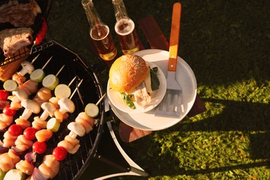 Photo of Tasty burger on table near barbecue grill outdoors, flat lay