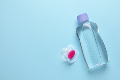 Bottle of baby oil and pacifier on light blue background, flat lay. Space for text