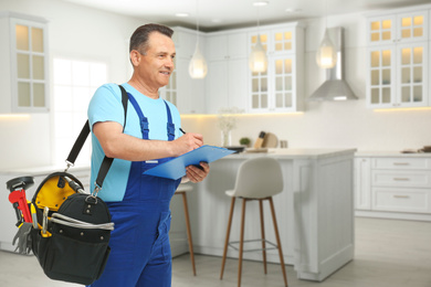 Mature plumber with clipboard and tool bag in kitchen, space for text