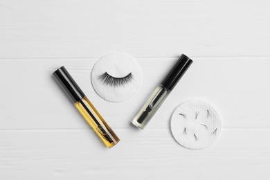 Photo of False eyelashes and tubes of different oils on white wooden table, flat lay