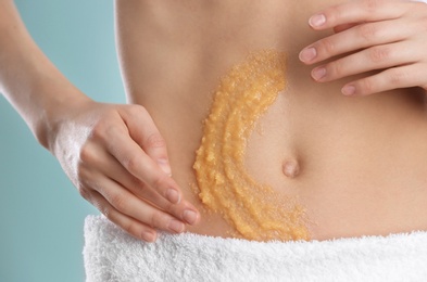 Young woman applying natural scrub on her belly against color background, closeup