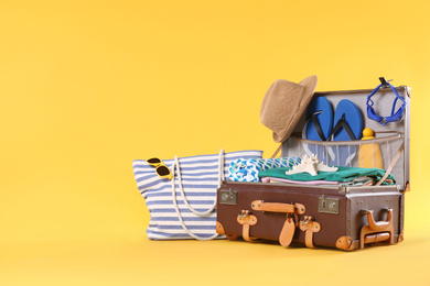 Bag and packed vintage suitcase with different beach objects on orange background, space for text. Summer vacation