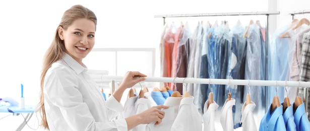 Young woman near rack with clean clothes, banner design. Dry-cleaning service