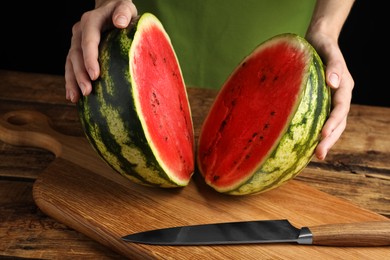 Woman with delicious halved watermelon at wooden table against black background, closeup