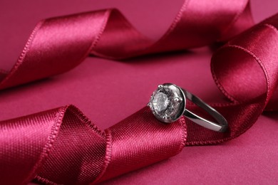 Beautiful luxury engagement ring with gemstone and ribbons on marsala background, closeup