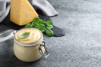 Photo of Tasty cheese sauce with basil in glass jar on grey table, space for text