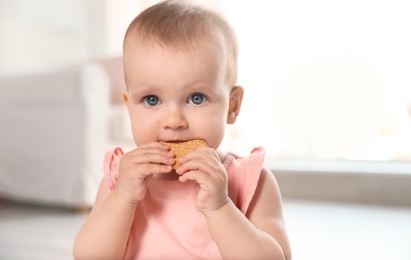 Portrait of cute baby girl with cookie in room