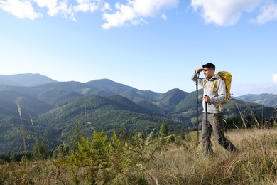 Tourist with backpack and trekking poles enjoying mountain landscape, space for text