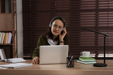 Woman with modern laptop and headphones learning at table indoors