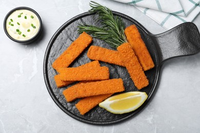 Fresh breaded fish fingers, sauce and lemon served on light grey table, flat lay