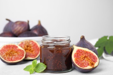 Glass jar of tasty sweet fig jam and fruits on light table