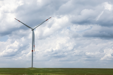 Photo of Modern wind turbine in field on cloudy day. Alternative energy source
