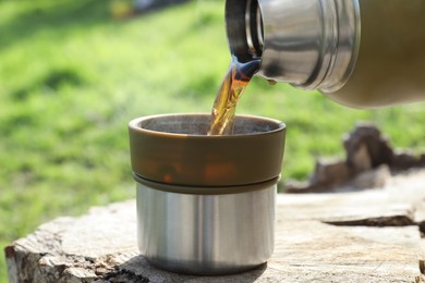 Pouring hot drink into mug on tree stump, closeup