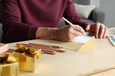 Man writing message in greeting card at wooden table, closeup