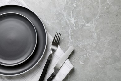 New dark plates, cutlery and napkin on light grey marble table, flat lay. Space for text