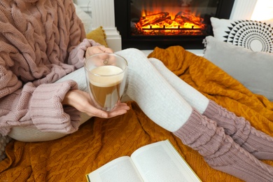 Woman with cup of coffee sitting near burning fireplace, closeup