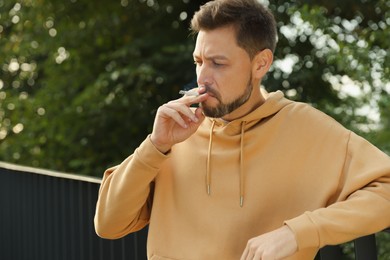 Photo of Man smoking cigarette near railing outdoors. Bad habit