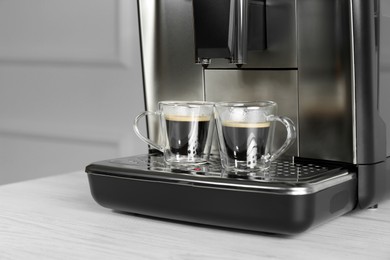 Modern espresso machine with cups of coffee on white wooden table, closeup