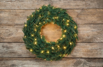 Christmas wreath made of fir branches with string lights on wooden background, top view