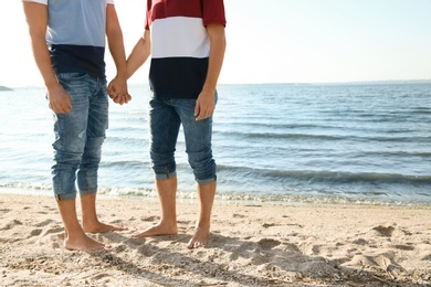 Gay couple standing barefoot on beach. Space for text