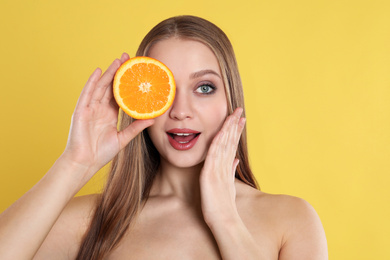 Photo of Young woman with cut orange on yellow background. Vitamin rich food