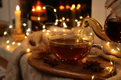 Photo of Pouring aromatic anise tea into glass cup on wooden board indoors, bokeh effect
