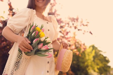 Young woman with bouquet of tulips and hat in park on sunny day, closeup. Space for text