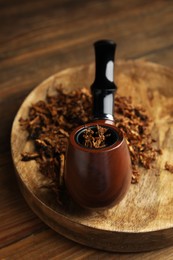 Board with smoking pipe and dry tobacco on wooden table, closeup