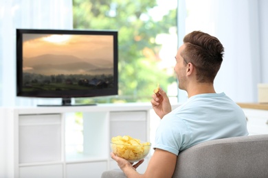 Photo of Man eating potato chips while watching TV in living room
