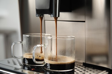 Espresso machine pouring coffee into glass cups against blurred background, closeup