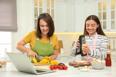 Mother with adult daughter making dinner while watching online cooking course via laptop in kitchen