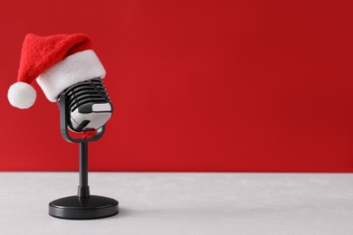 Retro microphone with Santa hat on table against red background, space for text. Christmas music