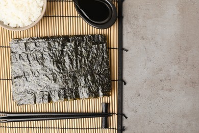 Dry nori sheets, rice, soy sauce and chopsticks on grey table, flat lay. Space for text