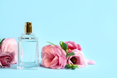 Bottle of perfume and beautiful flowers on light blue background. Space for text