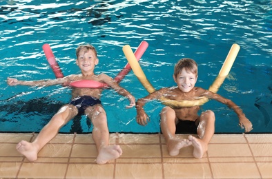 Little boys with swimming noodles in indoor pool