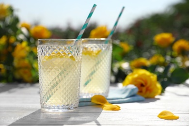 Glasses of refreshing lemonade on white wooden table in rose garden. Space for text