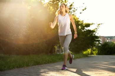 Young woman running in park on sunny day, space for text