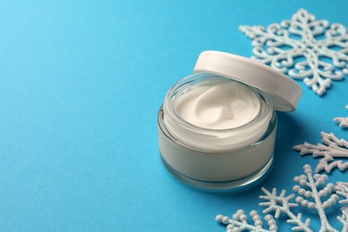 Photo of Jar of hand cream and snowflakes on light blue background, space for text. Winter skin care