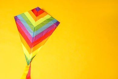 Bright rainbow kite on yellow background, top view. Space for text