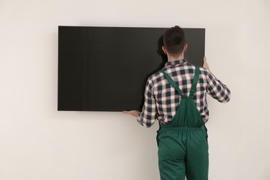 Professional technician installing modern flat screen TV on wall indoors, back view