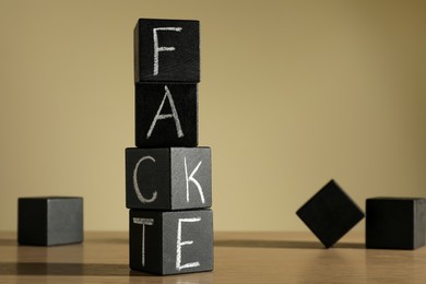 Photo of Words FAKE and FACT made with black cubes on wooden table, space for text