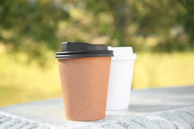 Photo of Cardboard cups with tasty coffee on stone bench outdoors, closeup
