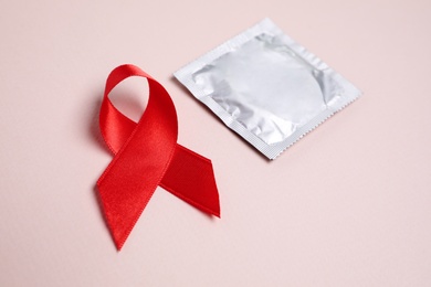 Red ribbon and condom on pink background, closeup. AIDS disease awareness