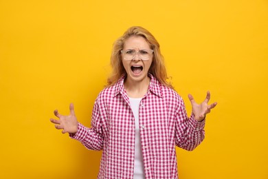 Photo of Aggressive young woman screaming with rage on yellow background