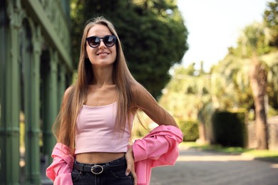 Beautiful young woman in stylish sunglasses on city street, space for text