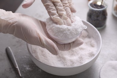 Photo of Woman in gloves making bath bomb at grey table, closeup