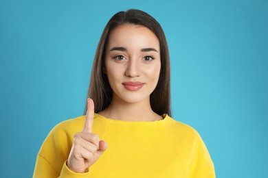 Woman showing number one with her hand on light blue background