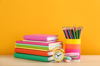 Different school stationery and alarm clock on table against orange background, space for text. Back to school