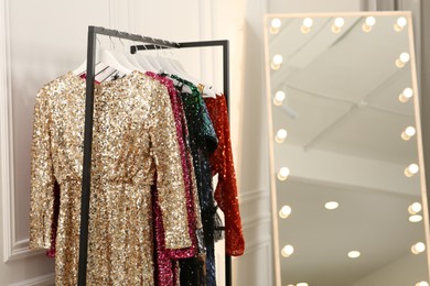 Photo of Clothing rack with colorful sequin party dresses on hangers near mirror in boutique, space for text
