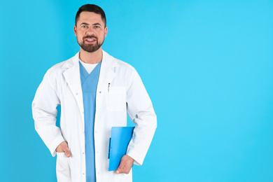 Portrait of mature doctor with clipboard against blue background, space for text